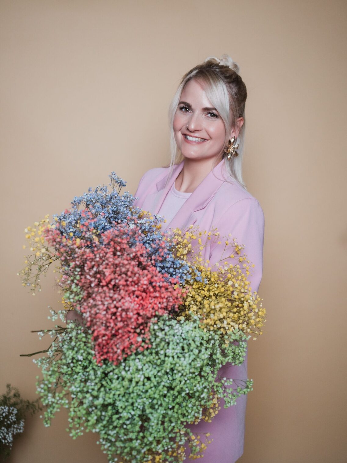 Woman in a pink blazer with green, yellow, pink and blue flowers in her hand