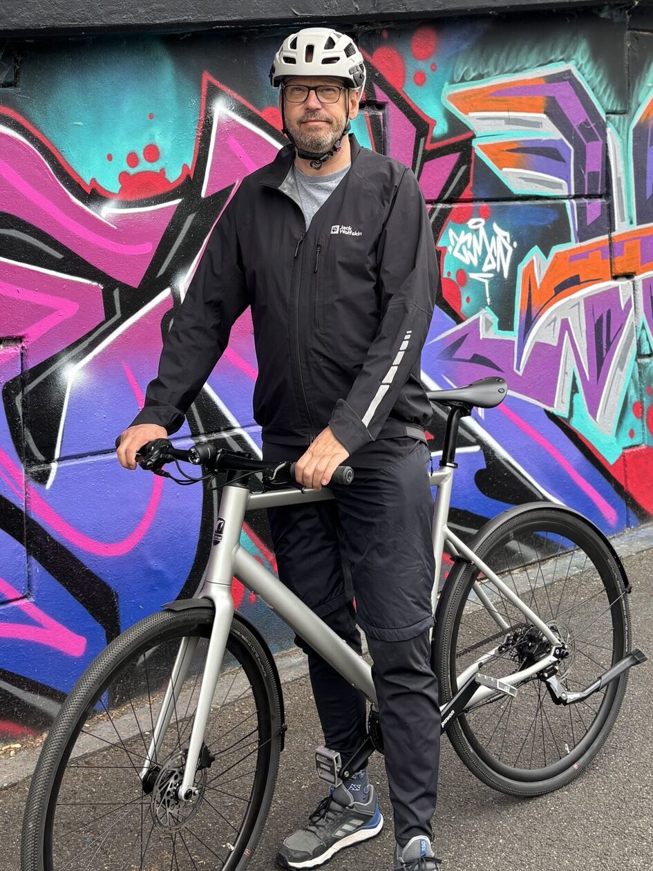 Mann mit Helm und Fahrrad vor einer Graffitiwand