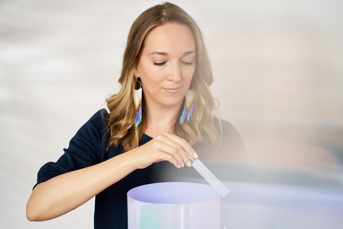 Frau mit bunten Ohrringen streicht mit einem Stab über den Rand eines Zylinders