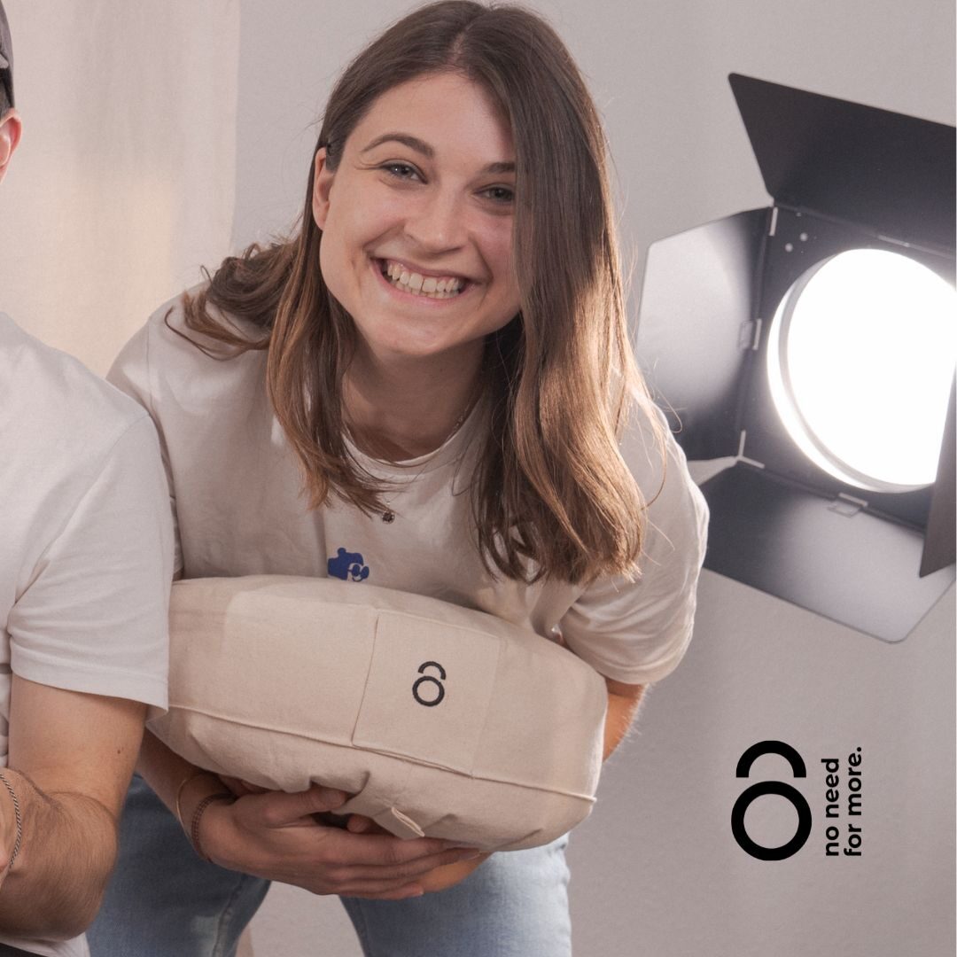 Eine Frau steht vornübergebeugt vor einem Filmlicht und lacht ein Textilobjekt mit beiden Armen haltend in die Kamera