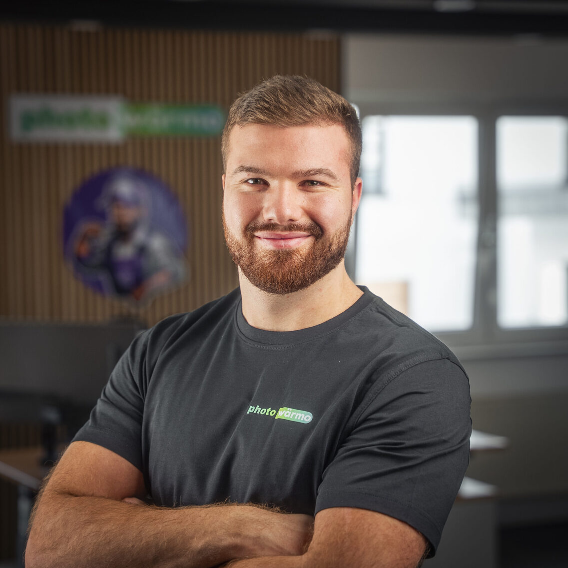 Un bărbat stă cu brațele încrucișate și zâmbește în fața camerei