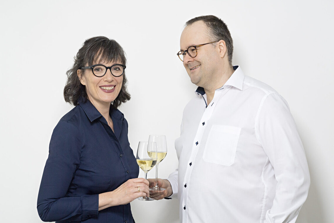 eine Frau und ein Mann stehen zueinandergewandt und halten jeweils ein gefülltes Weinglas