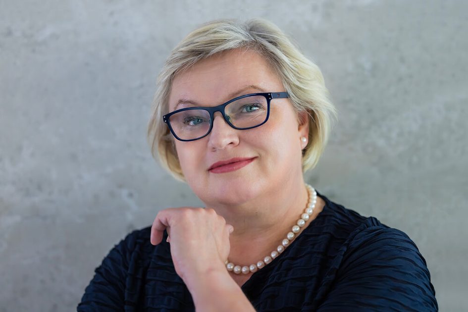 Frau mit Brille, blonden Haaren und schwarzer Jacke.