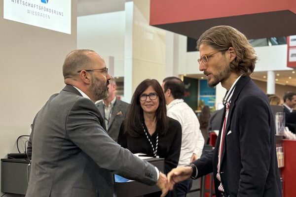 drei Mitarbeitende des Referats für Wirtschaft und Beschäftigung der LHW stehen am Stand der LHW auf der EXPO REAL 2025 und besprechen sich über ein Dokument gebeugt