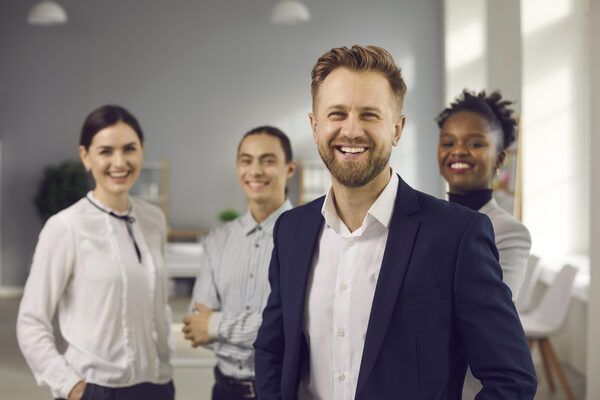 Happy startup CEO with team of employees standing in office and smiling at camera