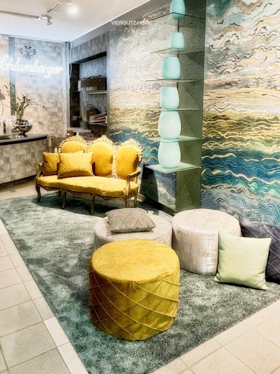 Σύνθεση από διάφορα διακοσμητικά αντικείμενα, μεταξύ των οποίων ένας καναπές, κύλινδροι καθισμάτων και ράφια, σε κίτρινους, γκρι και πράσινους τόνους.