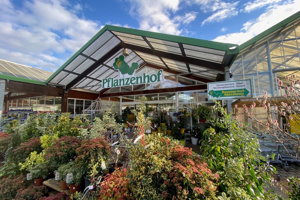 Стъклена къща с много зеленина отпред.