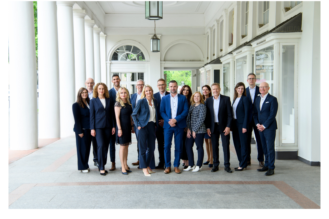 Eine Gruppe von Mitarbeitenden posiert für ein gemeinsames Foto in den Kolonnaden des Kurhauses.