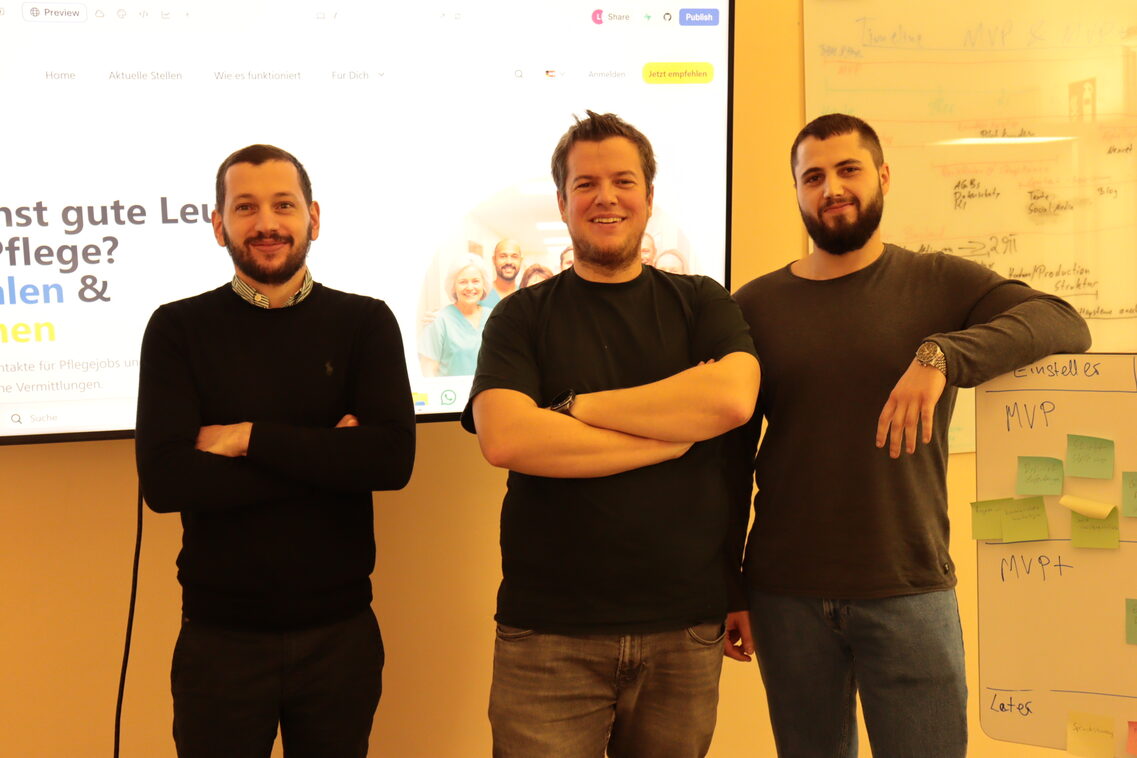 drei Männer stehen vor einem Bildschirm und lächeln