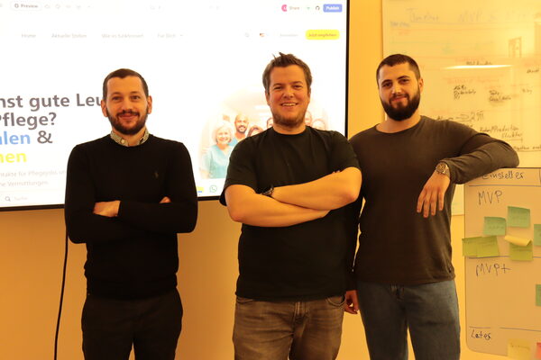 трима мъже стоят пред екран и се усмихват