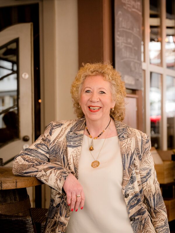 dirseğini ahşap bir bar masasına gevşekçe dayayarak kameraya gülen şık giyimli bayan