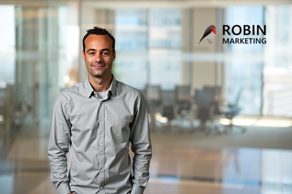 Ein Mann steht vor einem Besprechungsraum und schaut freundlich in die Kamera.